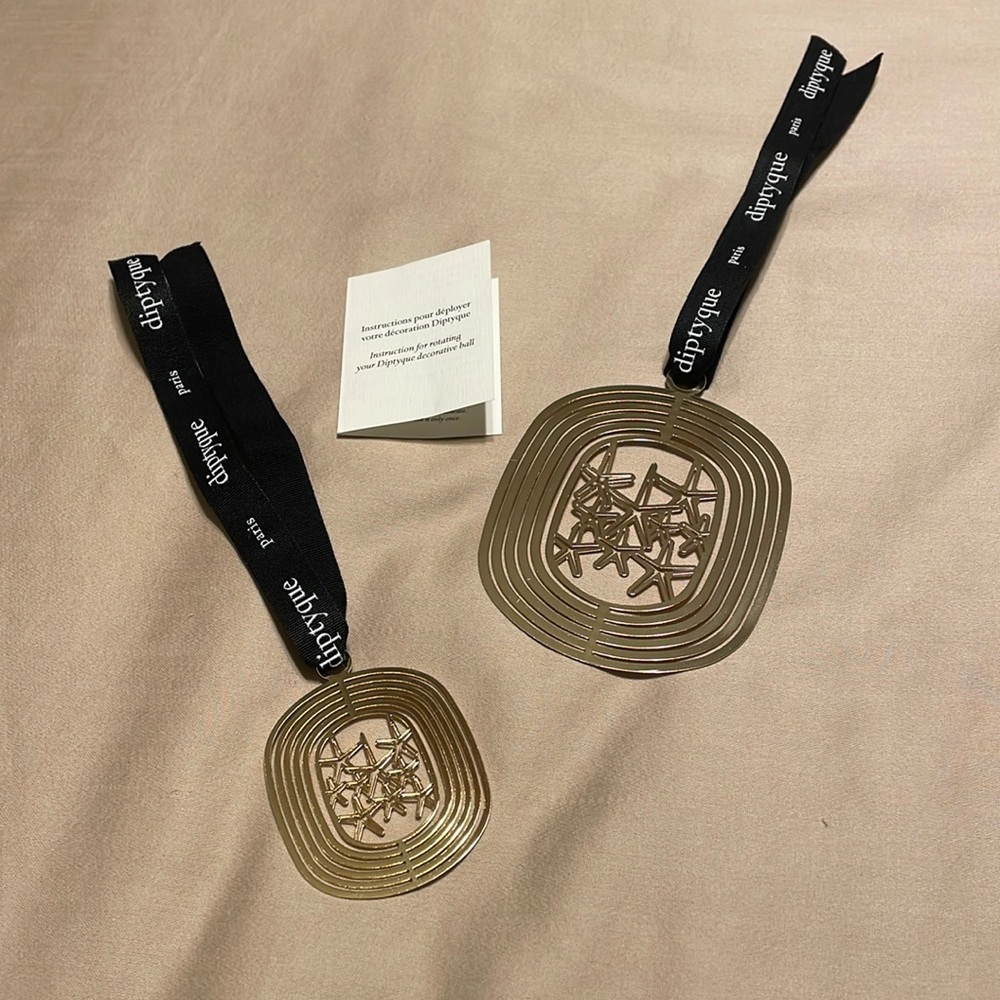 Diptyque set of two gold metal holiday ornaments with starfish details at center